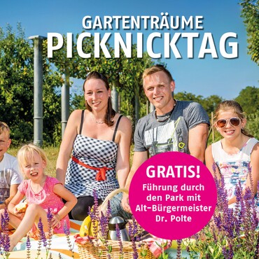 Familie picknickt auf einer Grünen Wiese des Elbauenparks. Im Hintergrund sieht man die Streuobstwiese.